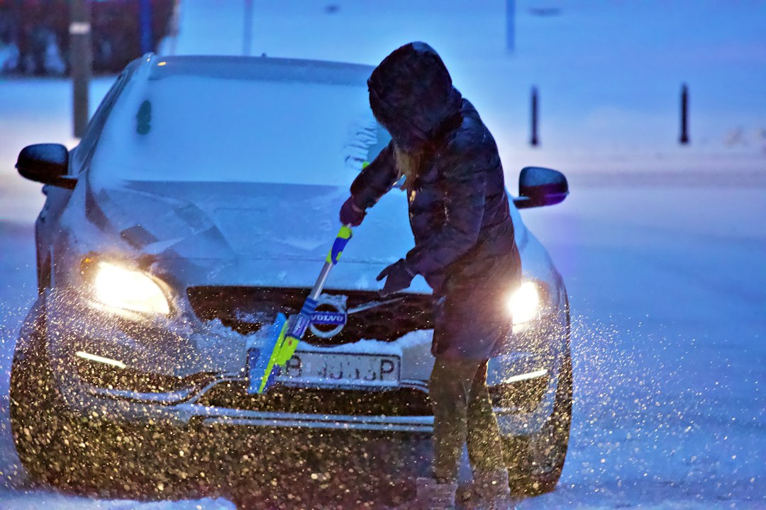 Person scraping frost from a car windshield on a winter morning